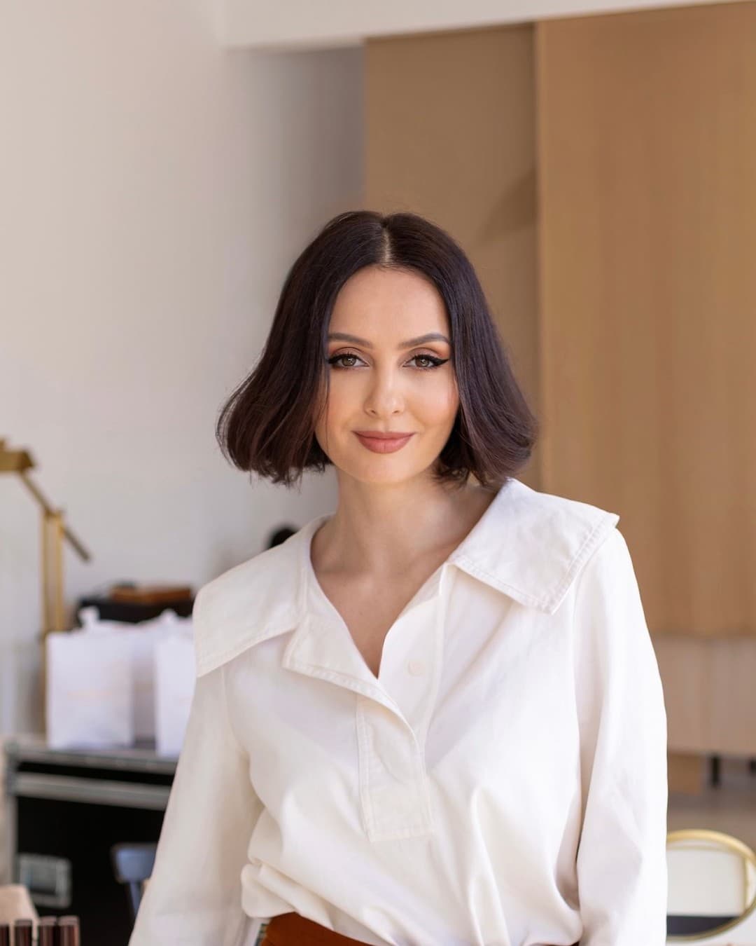 Tania Cozma, în cămașă albă, zâmbește într-un studio luminos în tonuri crem.